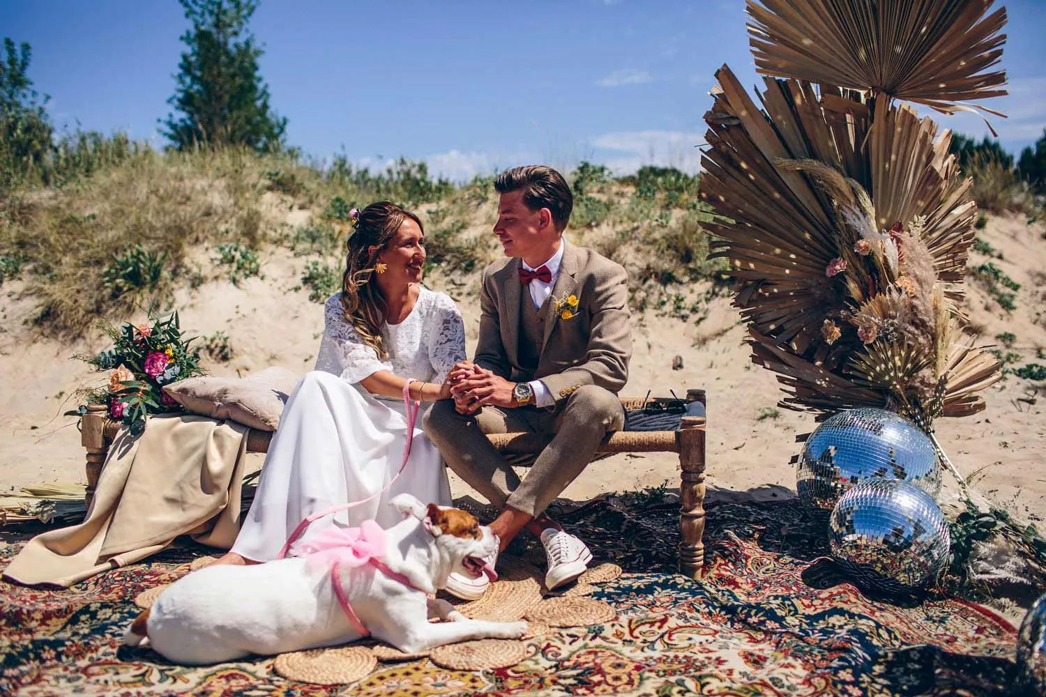 Pareja de novios sentada en una celebración en la playa junto a su perro